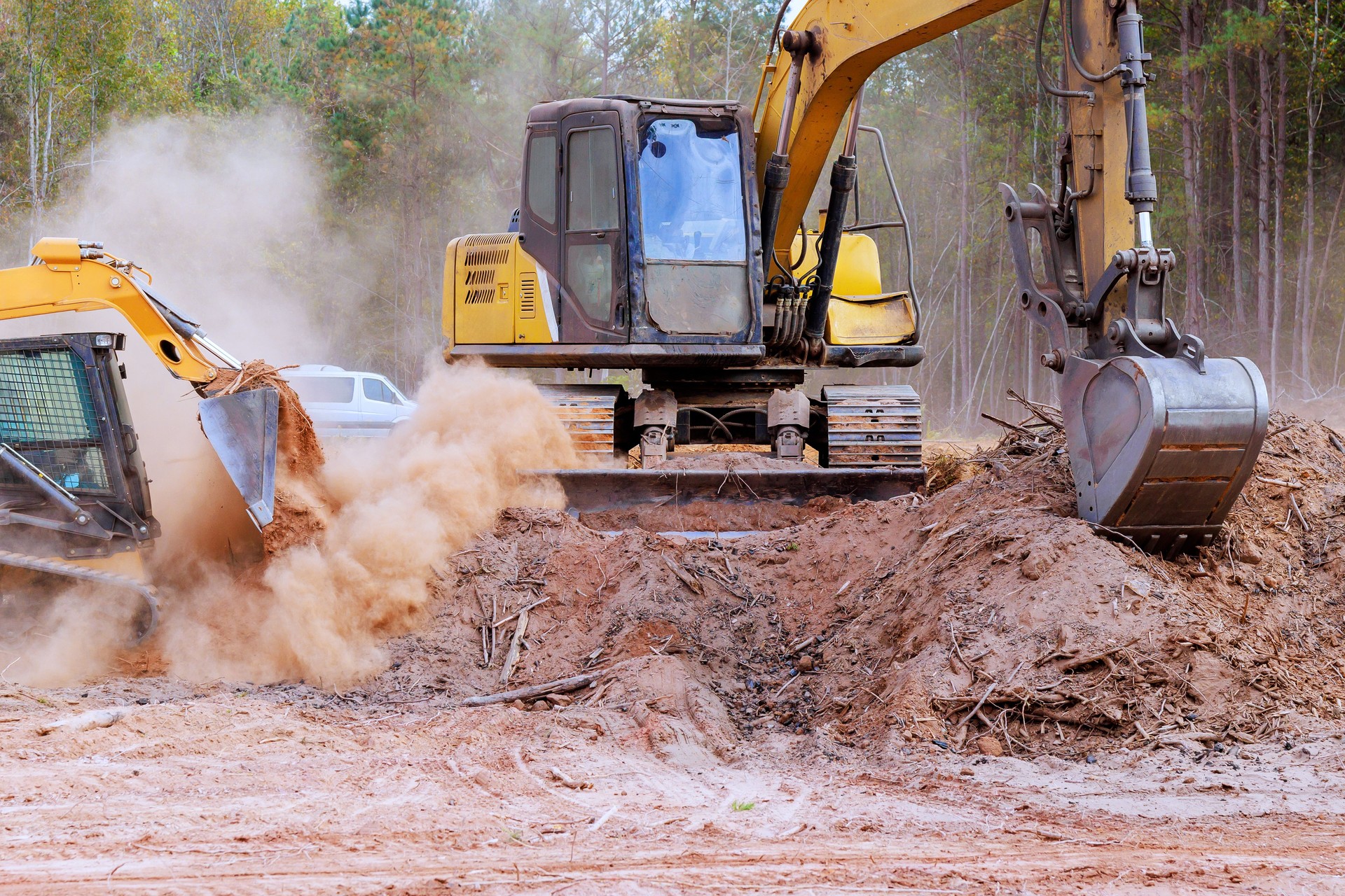 Construction machinery operates on job site clearing earth moving dirt during sunny day in forested area